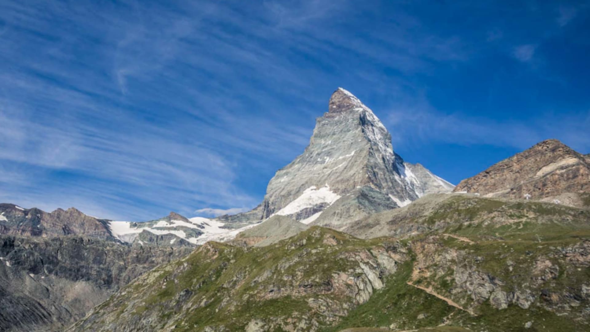 Blick auf die pyramidenförmige Felsspitze des Matterhorns mit sichtbaren Wanderwegen am Höhenrücken bei Zermatt.