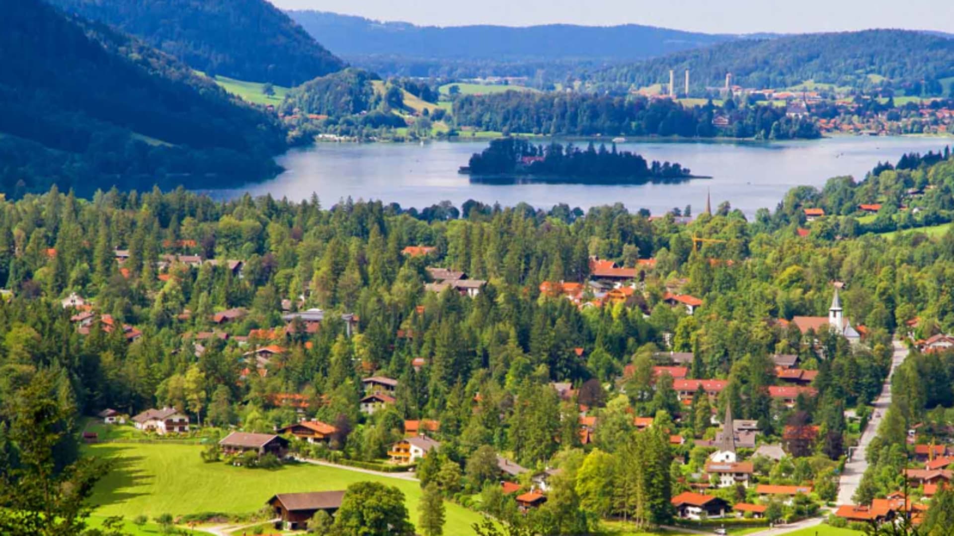 Bergwanderung am Schliersee: Panoramablick auf die Ortschaft mit Kirchtürmen und bewaldetem Seeufer im Sommer.