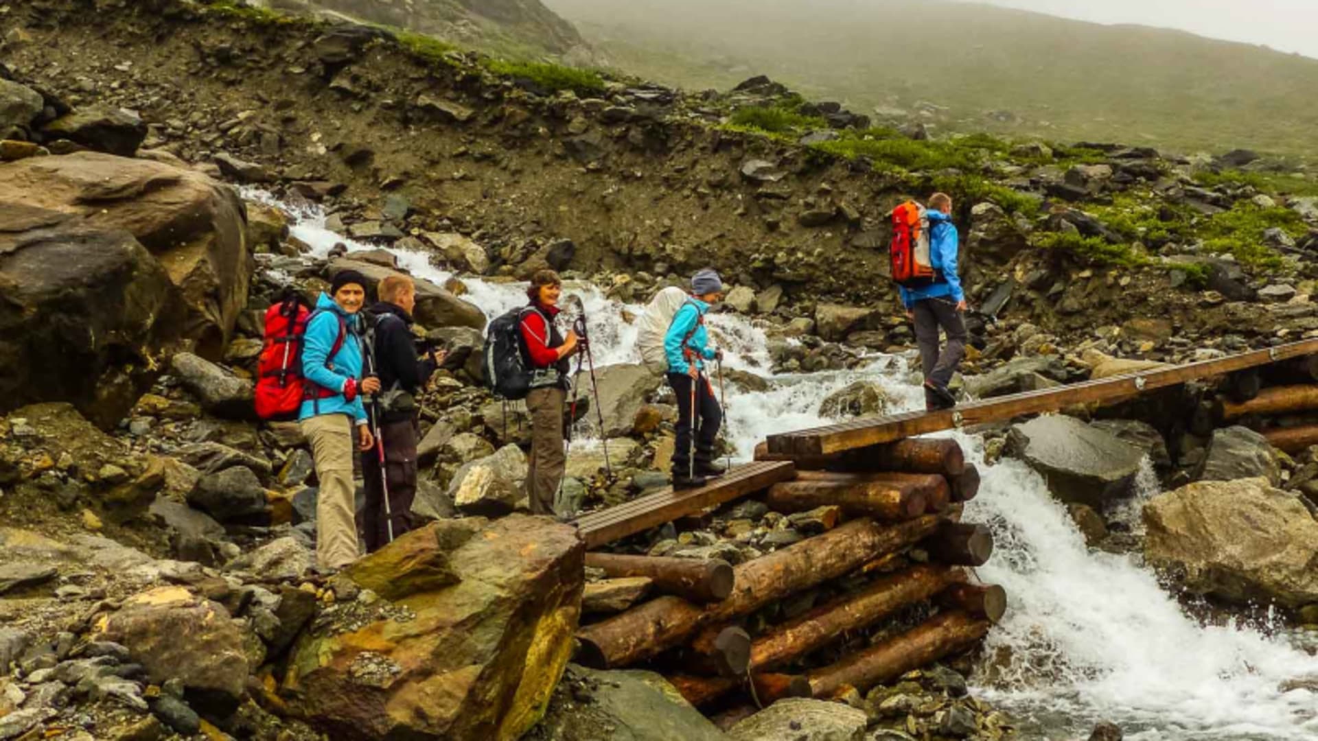Bergwanderung Hohe Tauern: Wanderergruppe überquert eine Holzstammbrücke über einen reißenden Wildbach bei der Hüttentour rund um