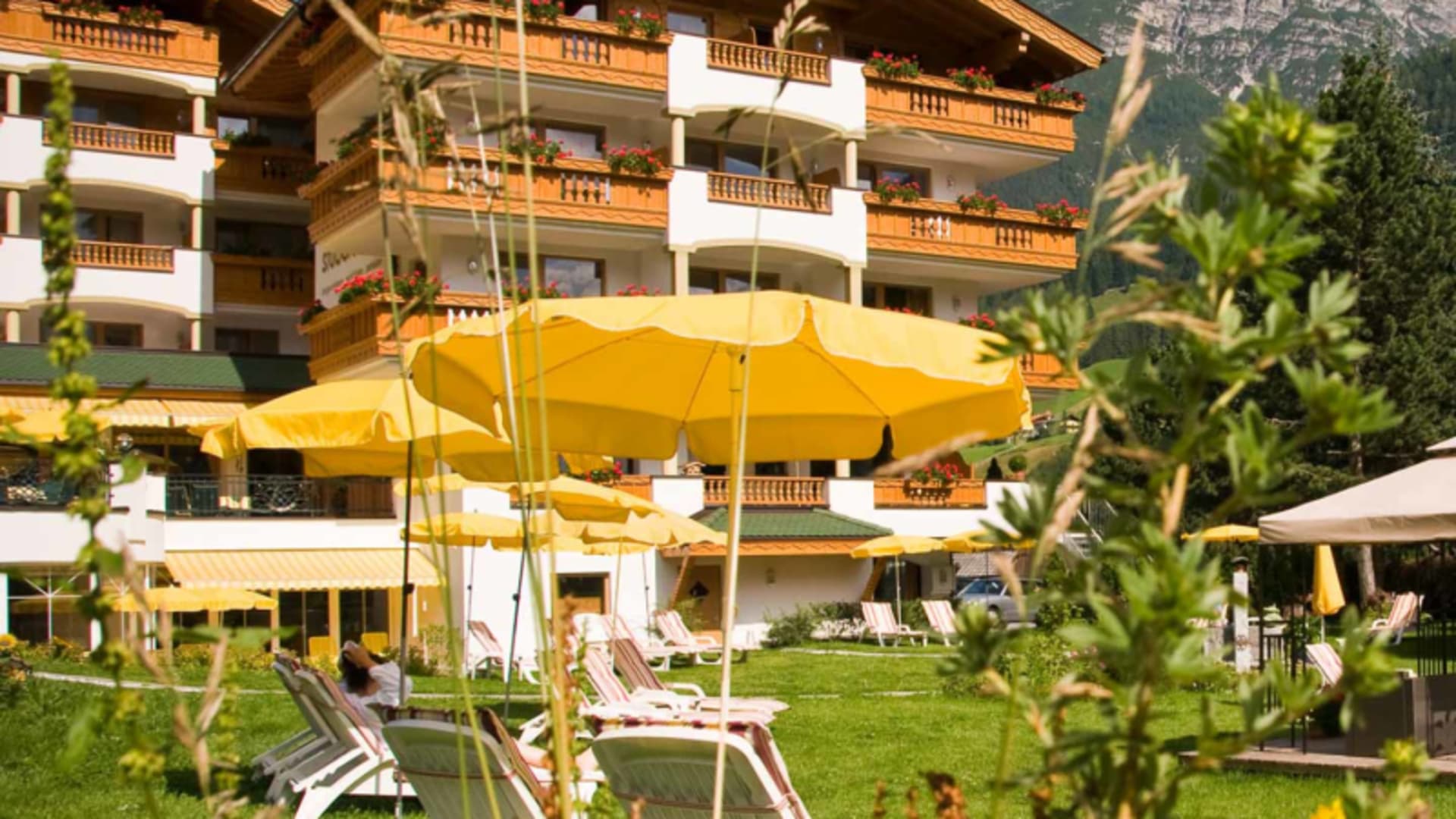 Stubaier Hof in Neustift zur Bergwanderung: Hotelgebäude im alpinen Stil mit Holzbalkonen, roten Blumenkästen und Liegestühlen