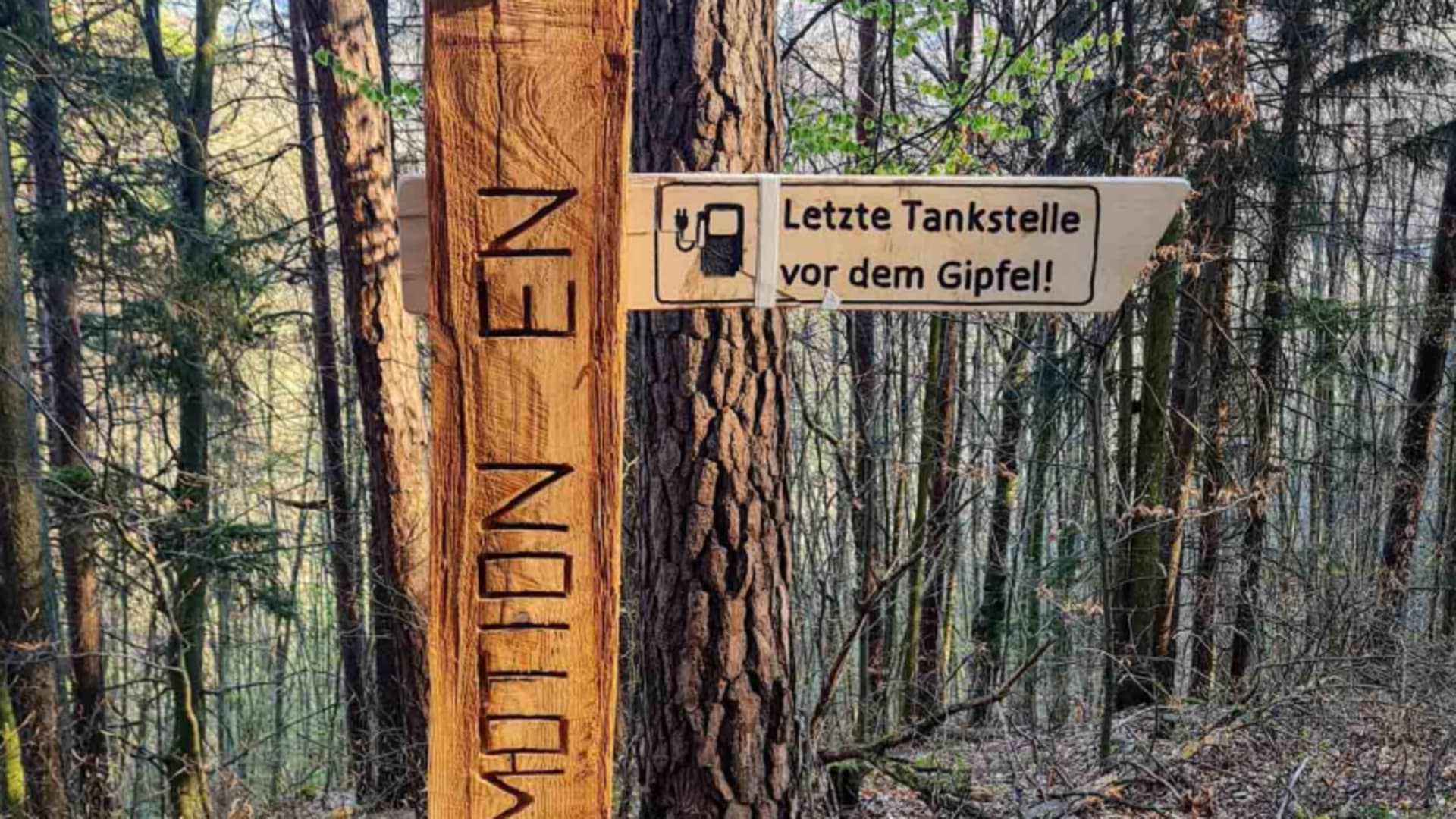 Bergwanderung Hersbrucker Schweiz: Holzwegweiser mit Aufschrift Letzte Tankstelle vor dem Gipfel an einem Holzpfosten im Laubwald.