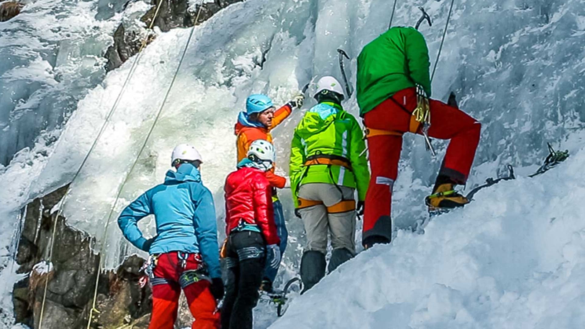 Eiskletterkurs: Fünf Personen trainieren Eisklettern-Technik an gefrorenem Wasserfall, eine gibt Anweisung