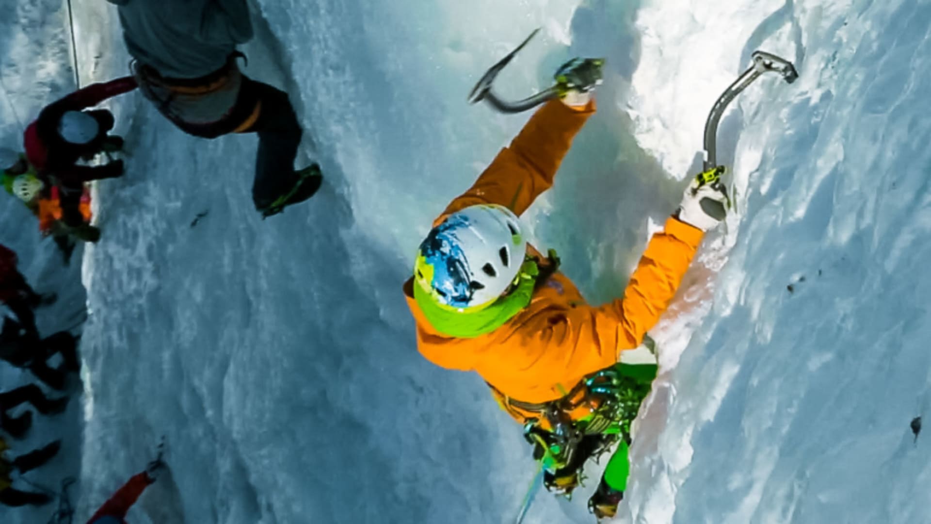 Eiskletterer im Vorstieg an senkrechter Eiswand mit Eisgeräten und Eisschrauben am Gurt, aufgenommen aus der Vogelperspektive.