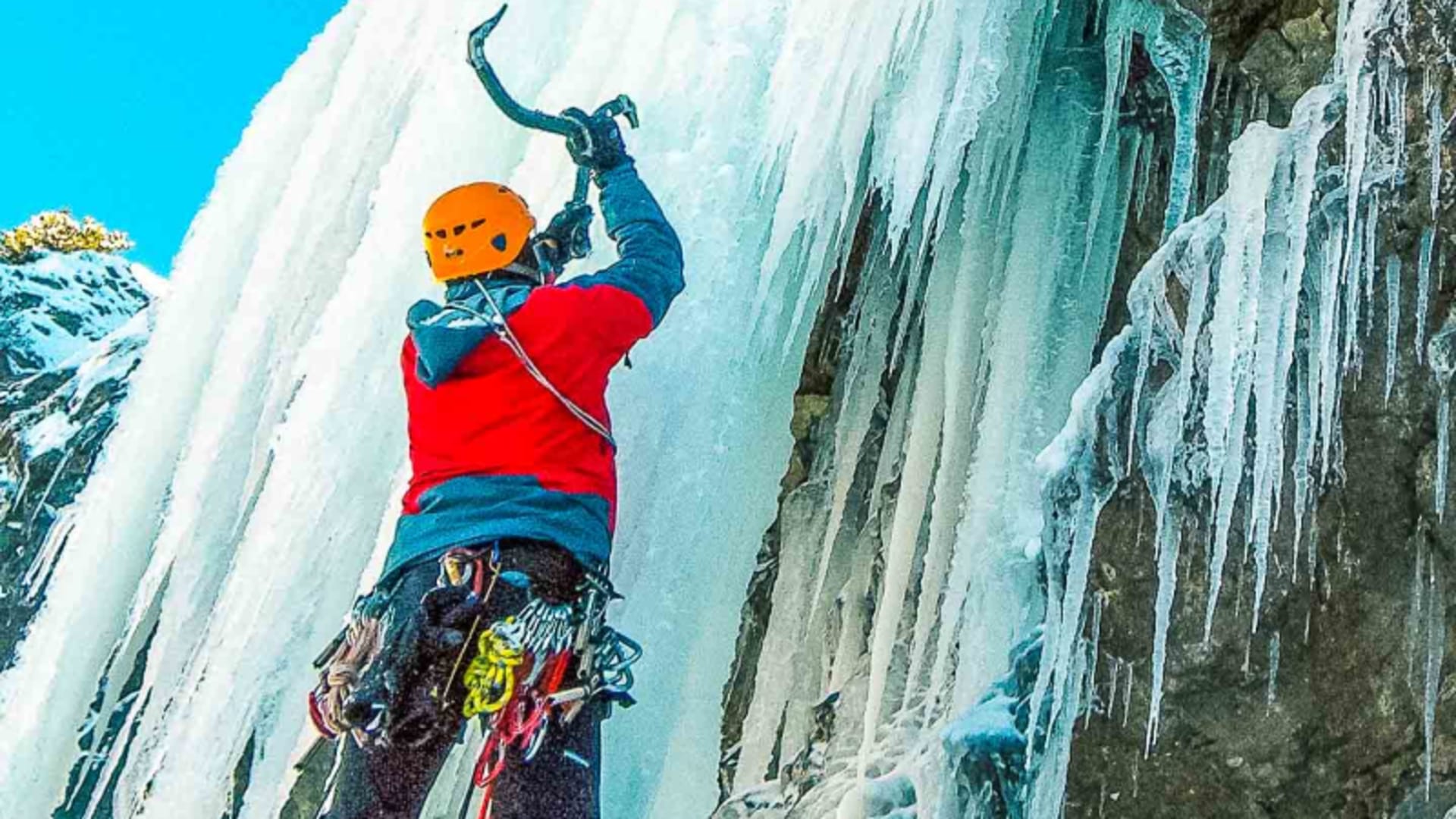 Eiskletterer schlägt mit zwei Eispickeln in eine senkrechte Eiswand an einem gefrorenen Wasserfall in den Dolomiten.