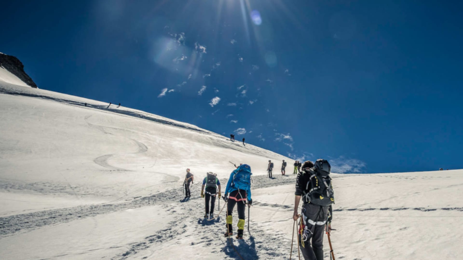 Bergsteigergruppe mit Steigeisen und Eispickel steigt in Reihe den Schneehang zum Allalinhorn auf.