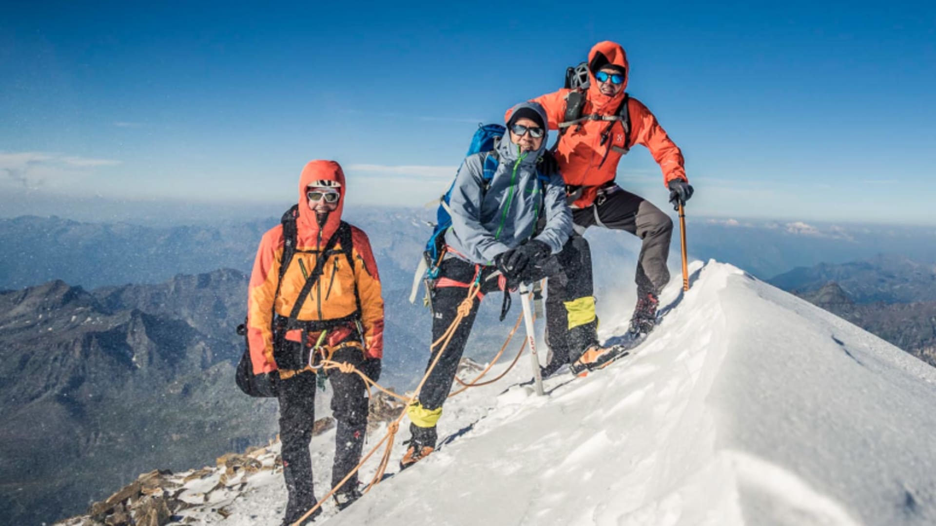 Drei Bergsteiger als Seilschaft auf dem schmalen Gipfelgrat des Gran Paradiso mit Steigeisen und Pickel.