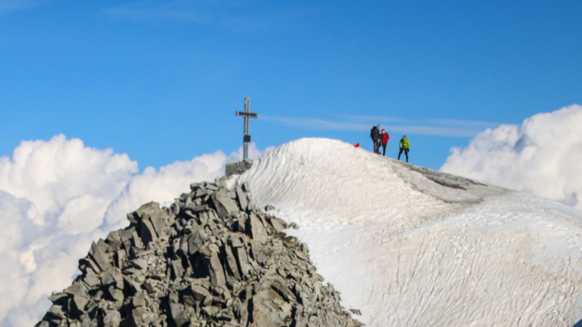 Hochtour auf den Großvenediger: drei Bergsteiger auf dem Schneegipfel neben dem Gipfelkreuz.