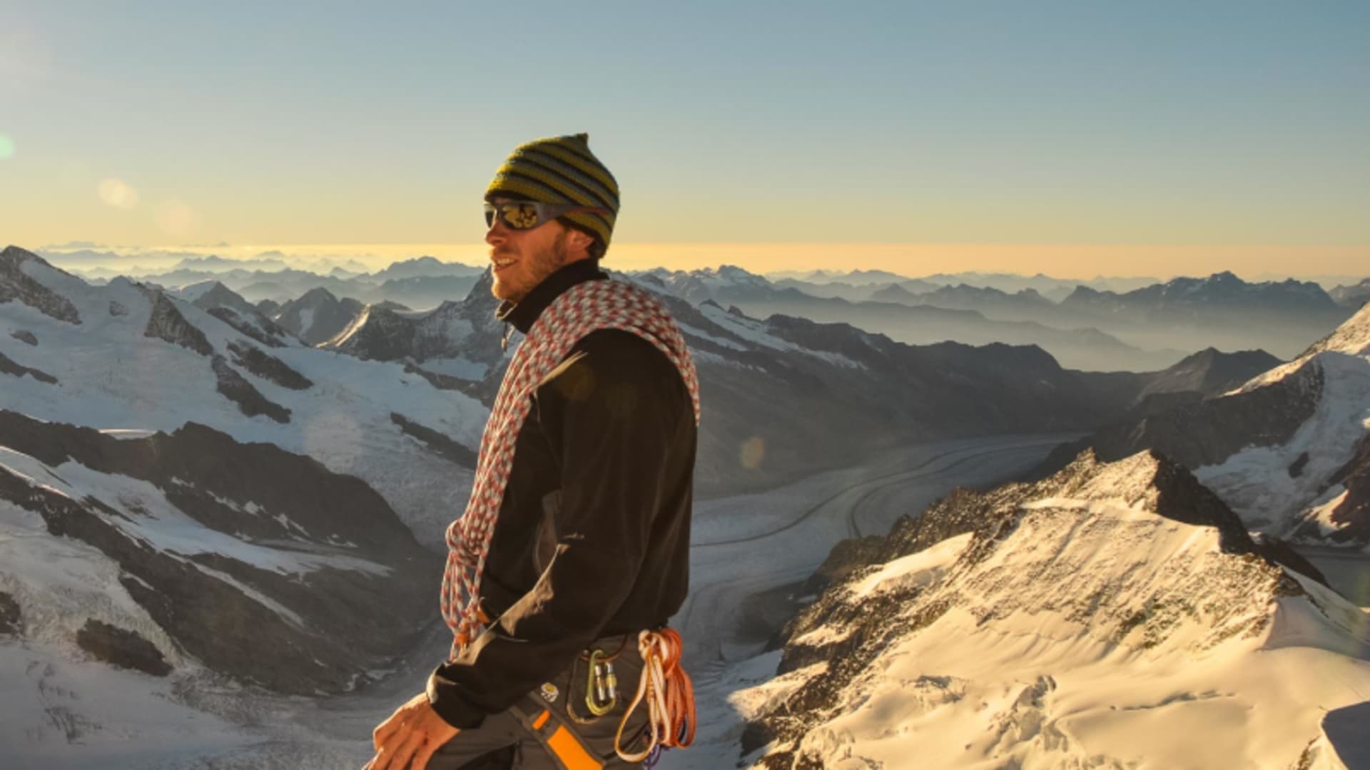 Bergsteiger mit Klettergurt und gelbem Seil auf dem Schneegrat der Jungfrau bei einer Hochtour, im Hintergrund weitläufiges