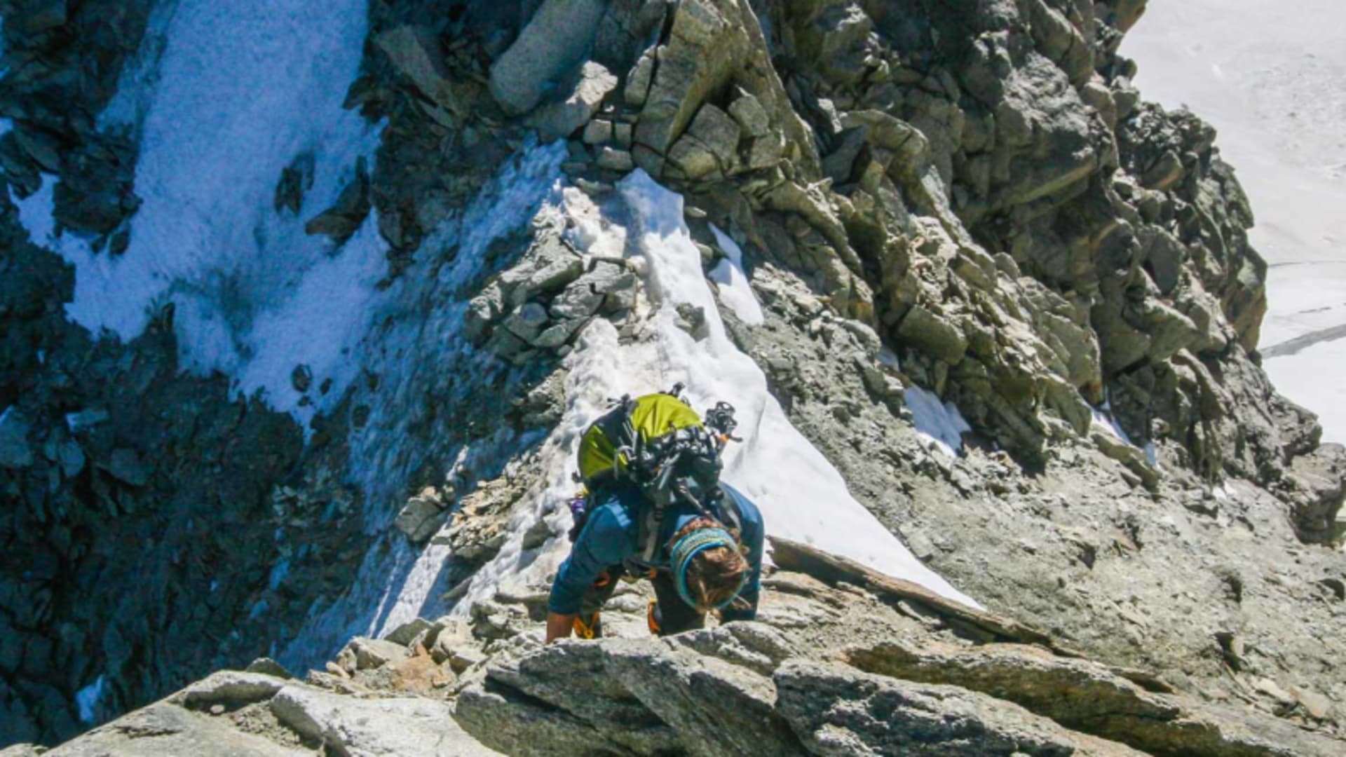 Zwei Bergsteiger steigen an einem schmalen Granitgrat im Mont-Blanc-Massiv auf, links steile Schnee- und Felswand.