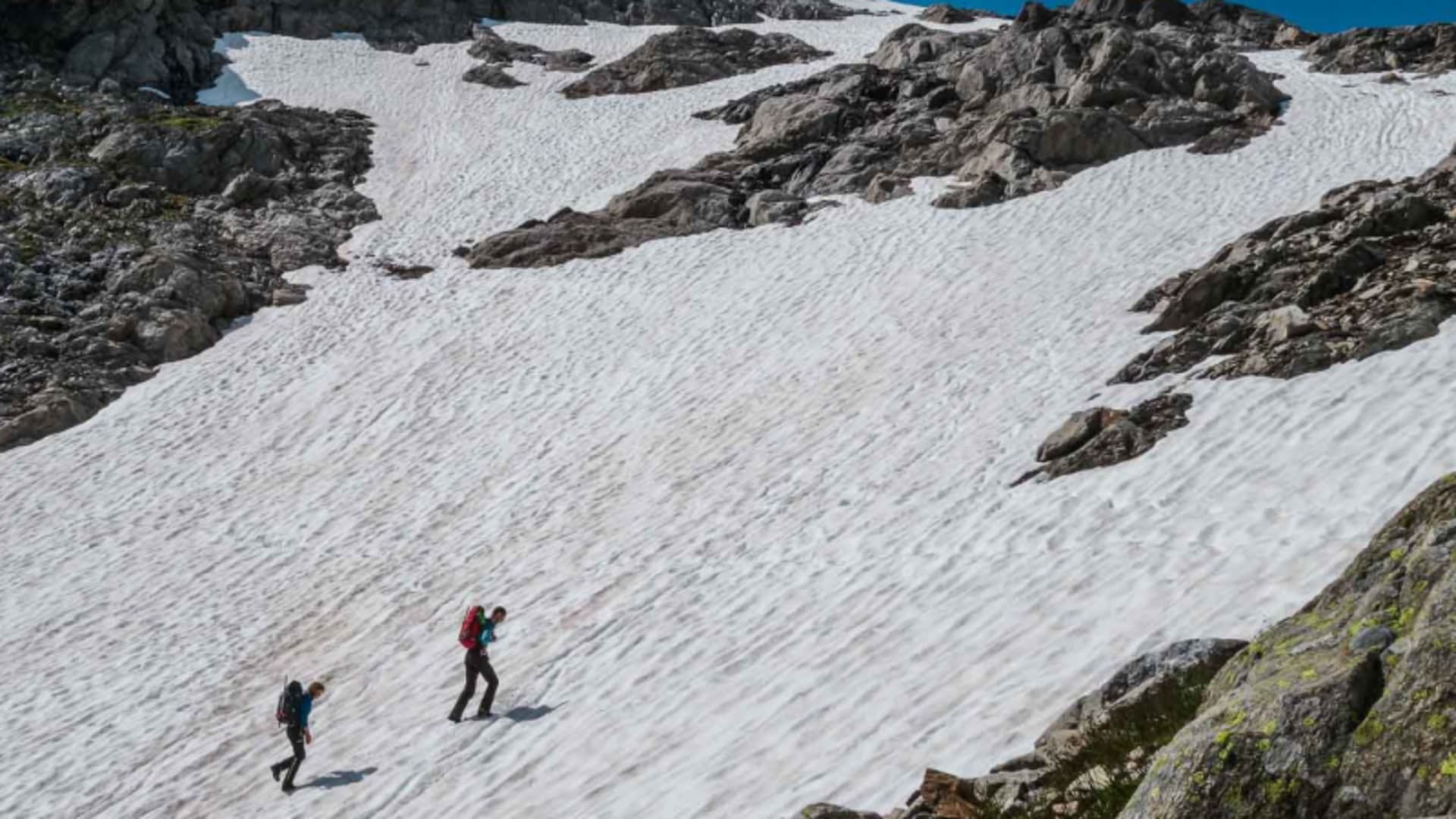 Zwei Bergsteiger queren im Hochtourenkurs einen ausgedehnten Firnhang zwischen Felsrippen im Hochgebirge.