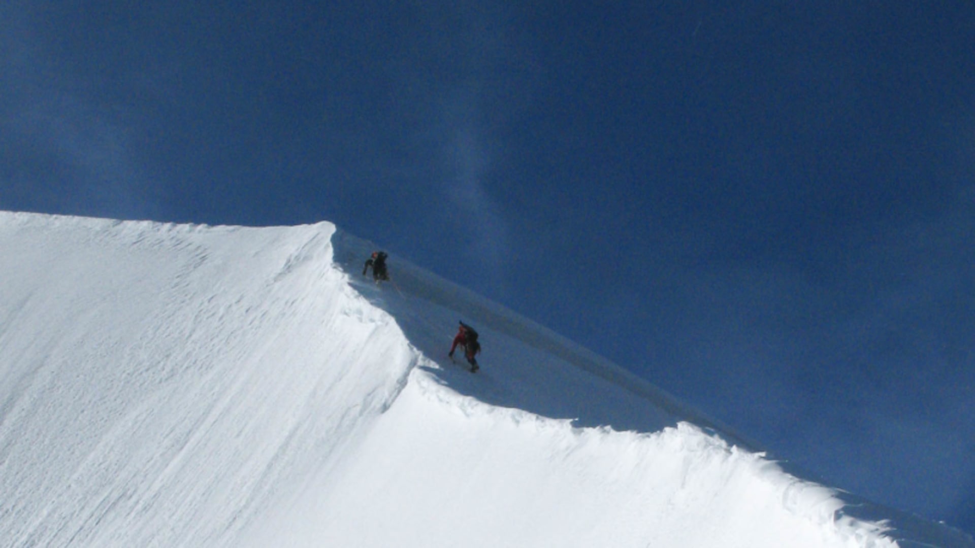Hochtour zum Piz Bianco: Drei Bergsteiger steigen auf einem schmalen Schneegrat mit Wächten aufwärts.