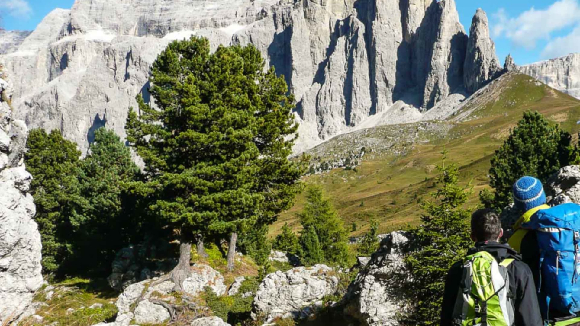 Zwei Kletterer mit Rucksäcken blicken auf die Kalksteinwand am Sellapass in den Dolomiten.