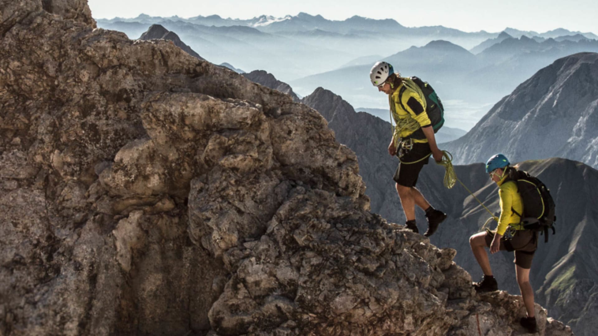 Zwei Kletterer steigen gesichert mit Seil am felsigen Jubiläumsgrat zur Zugspitze auf, Bergpanorama im Hintergrund.