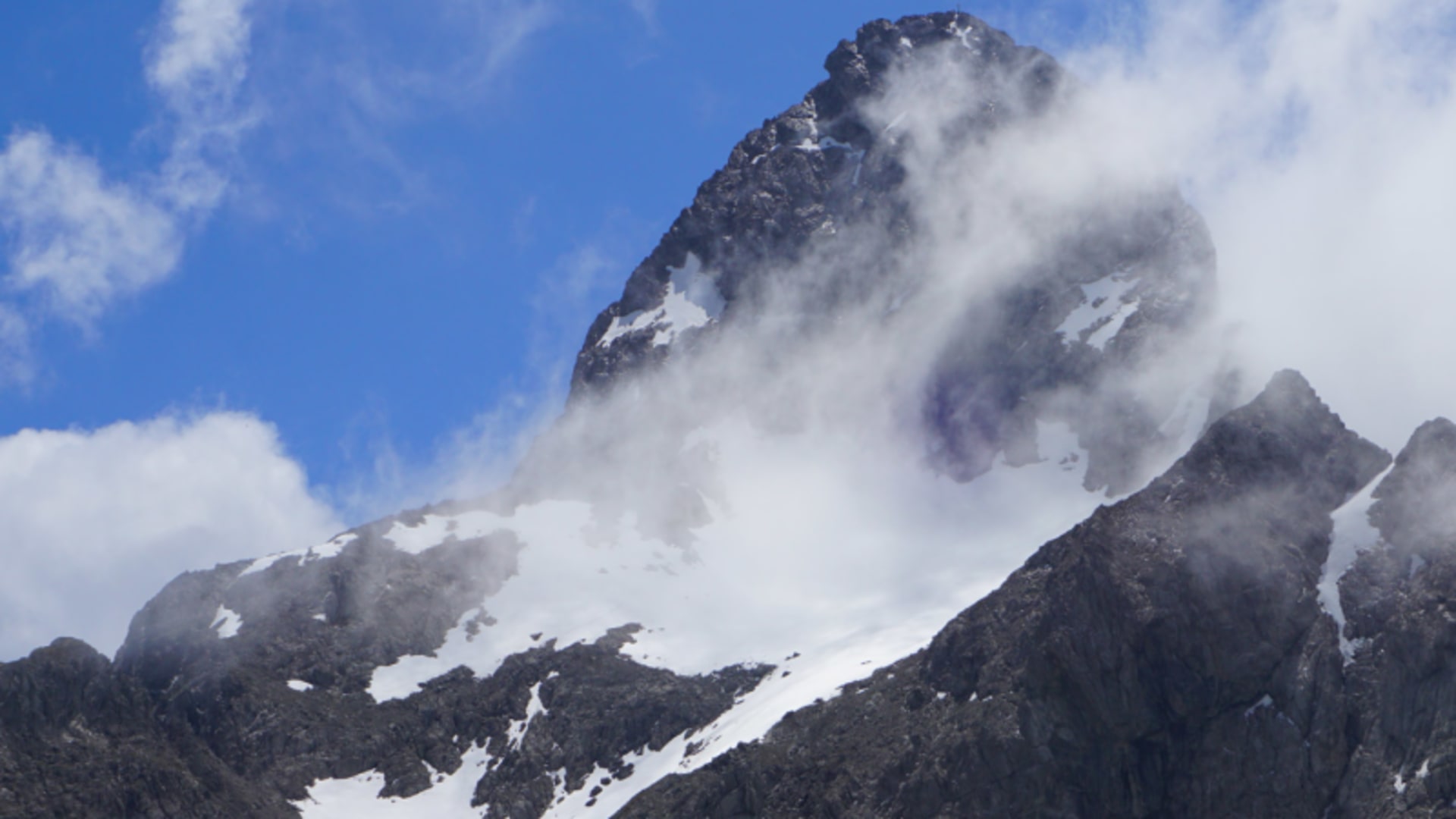 Zerklüfteter Felsaufbau der Trettachspitze beim Klettern, mit Restschnee in den Rinnen und Wolken am Gipfel