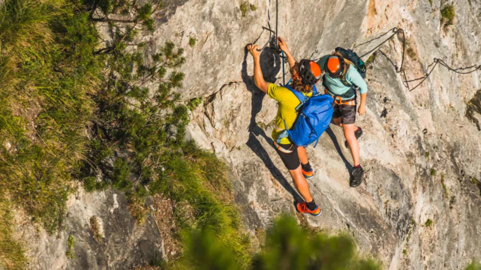 Zwei Klettersteiggeher greifen am Drahtseil einer glatten Kalkfelswand beim Klettersteig Berchtesgaden.
