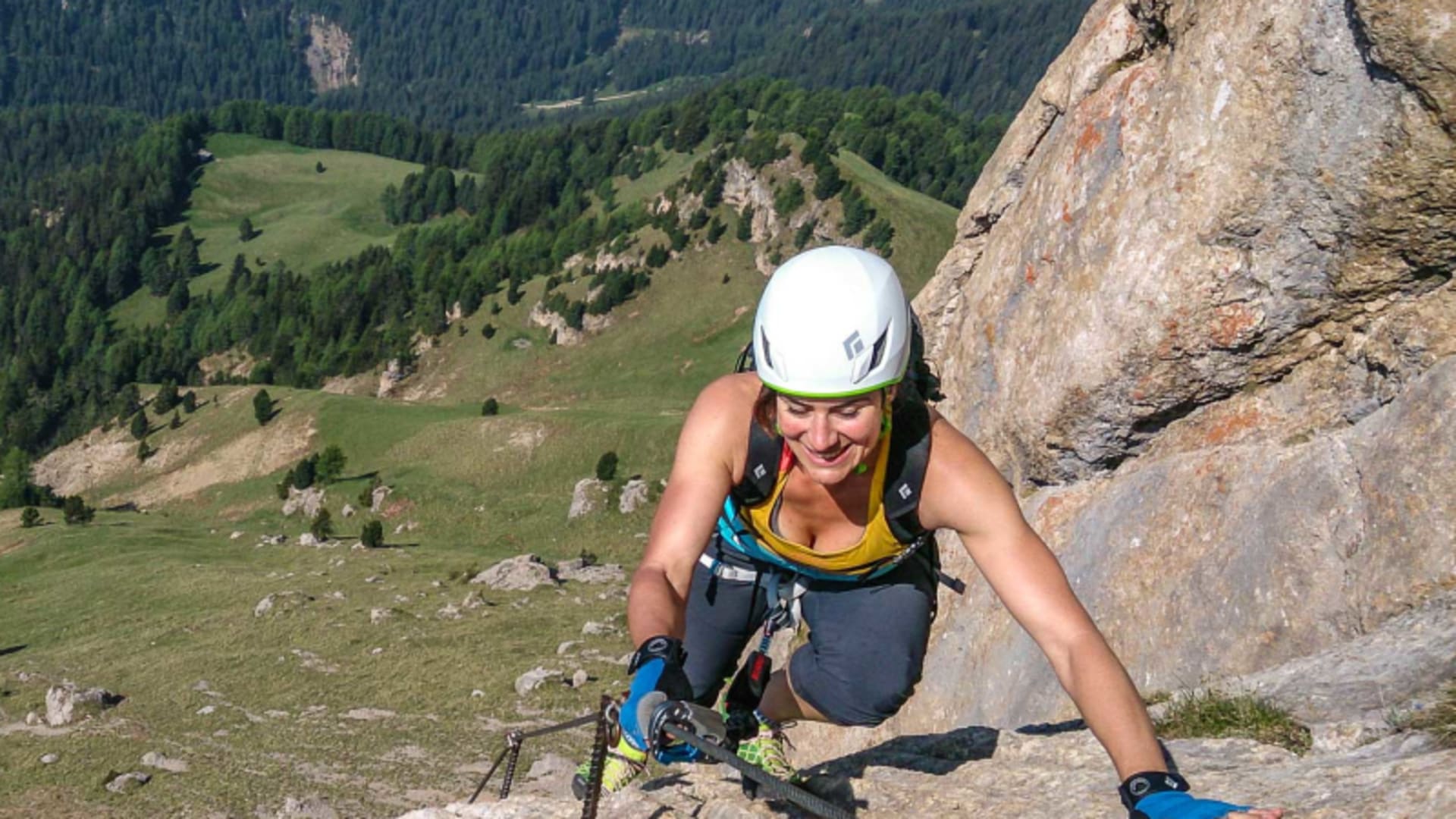 Kletterer mit weißem Helm und Klettersteigset steigt in den Dolomiten an Steigbügeln und Drahtseil einer steilen Felswand