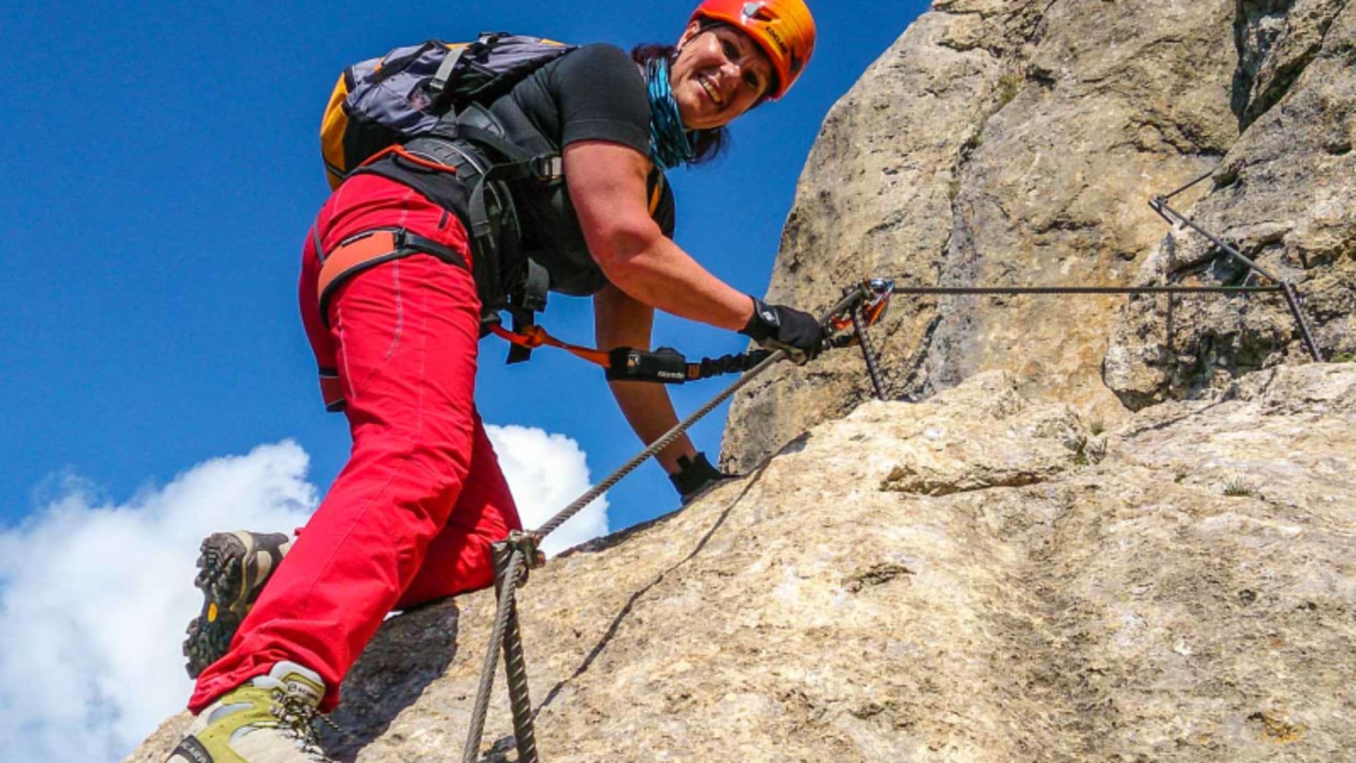 Klettersteiggeher mit orangenem Helm greift Fixseil an Kalkfelsplatte beim Klettersteig in Cortina d'Ampezzo.