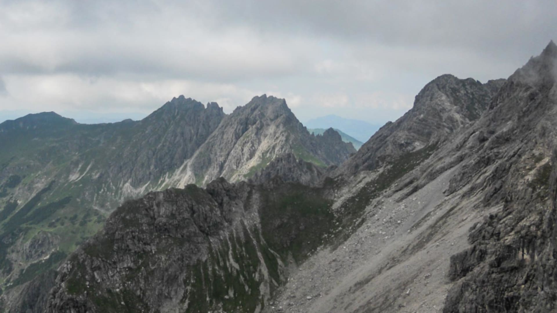 Panorama gezackter Felsgipfel und grüner Almhänge in den Allgäuer Alpen auf einem Klettersteig im Sommer.