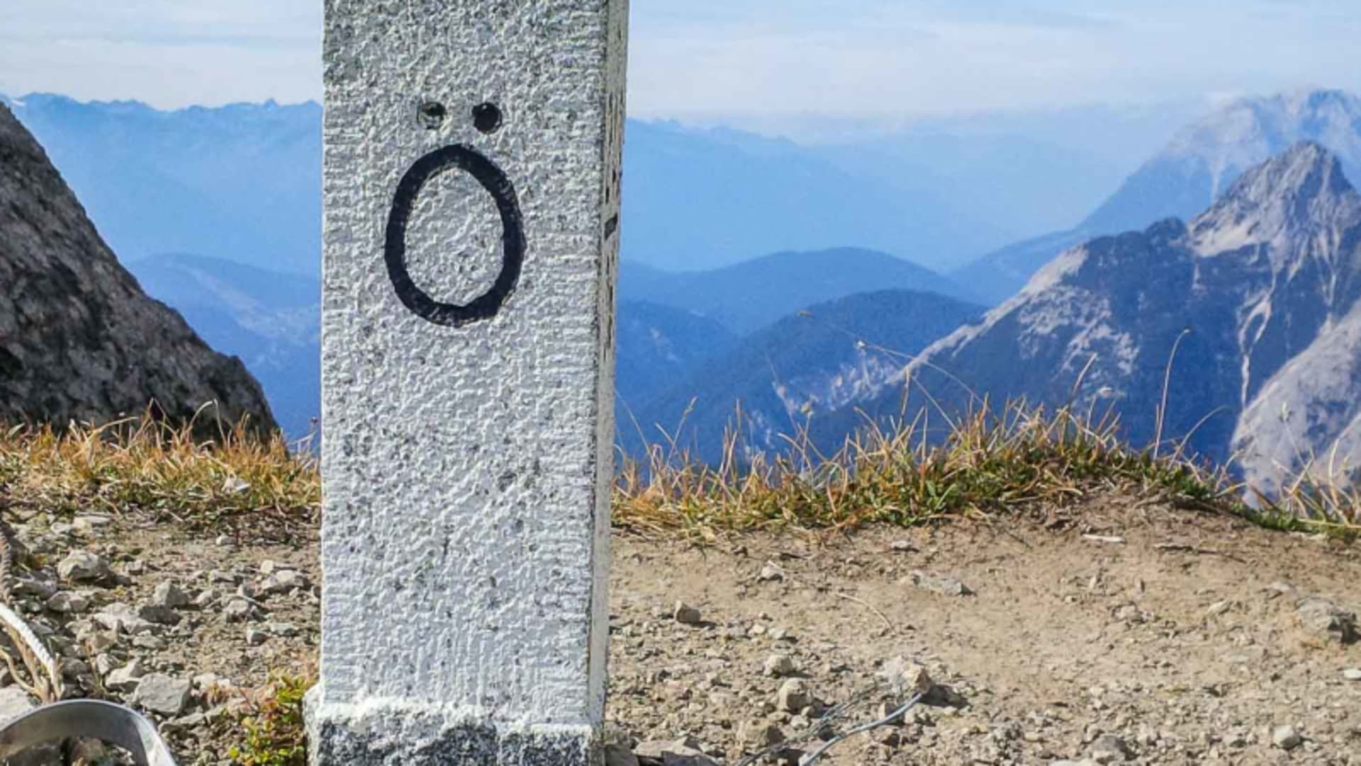 Klettersteig auf dem Mittenwalder Höhenweg: historischer Grenzstein aus Granit auf dem Bergrücken mit Kalksteingipfeln