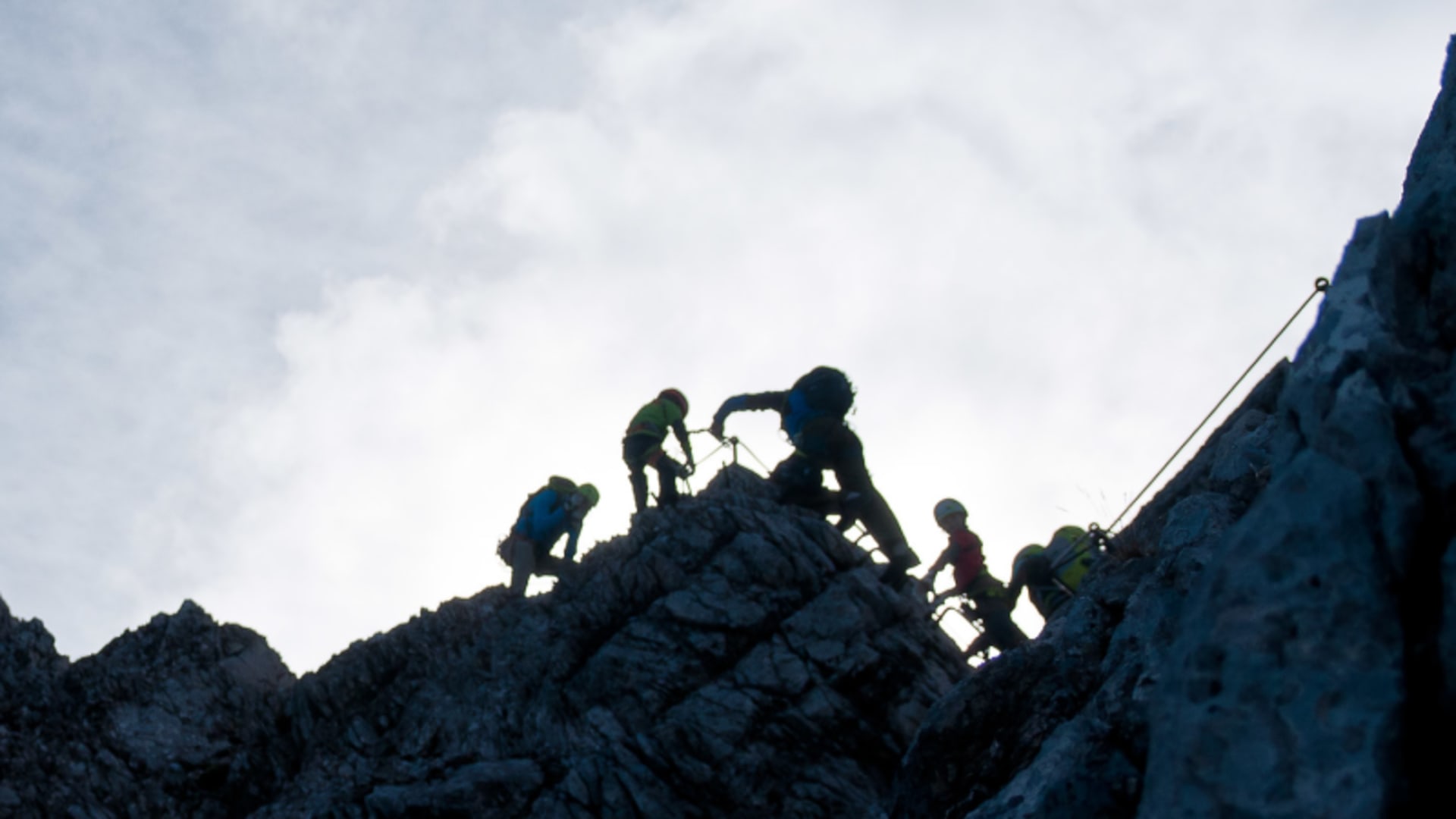 Fünf Klettersteiggeher steigen am Felsgrat der Alpspitze auf, gesichert an einem Stahlseil.