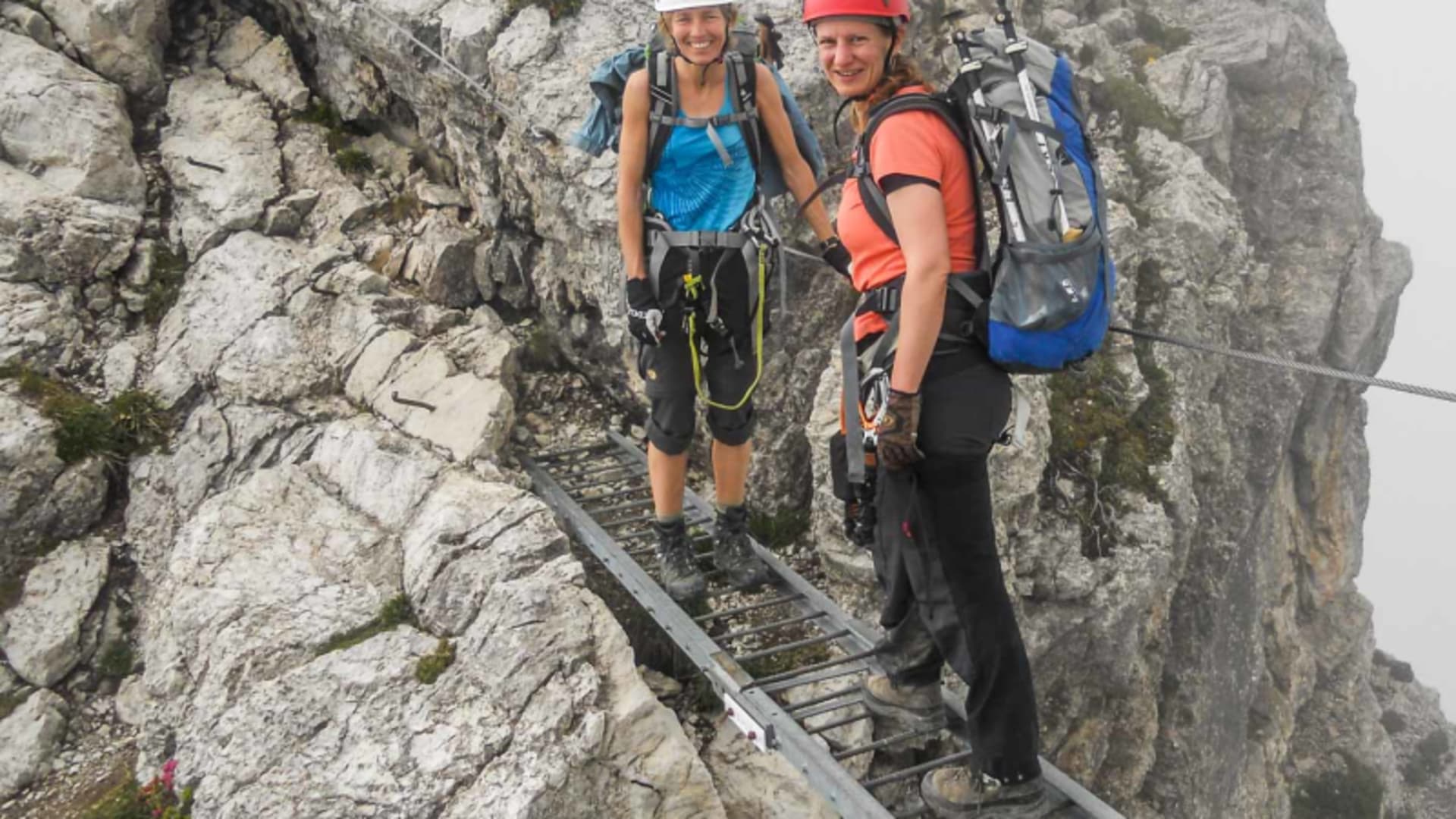 Zwei Klettersteiggeherinnen auf einer Metallleiter-Brücke am Mindelheimer Klettersteig im Allgäu.