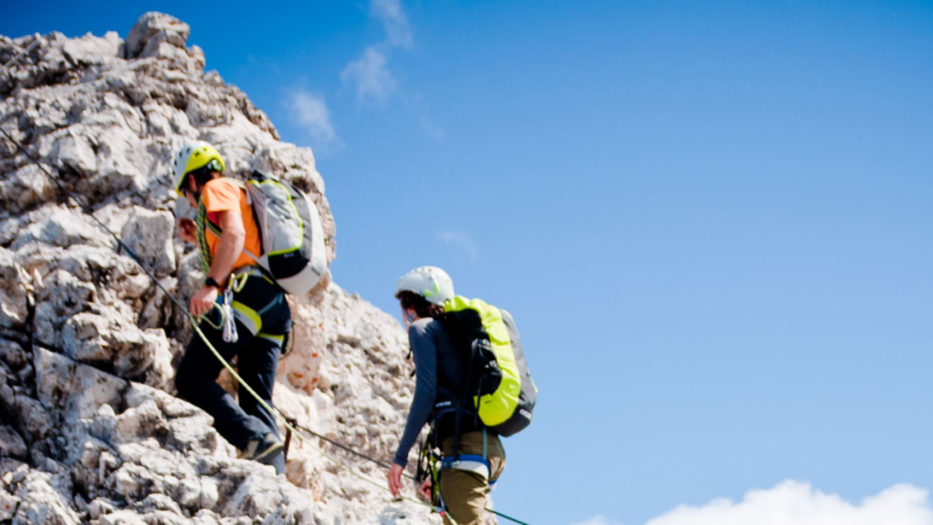 Zwei Teilnehmer eines Klettersteigkurses im Wettersteingebirge steigen mit Helm, Gurt und Rucksack eine helle Kalkfelswand