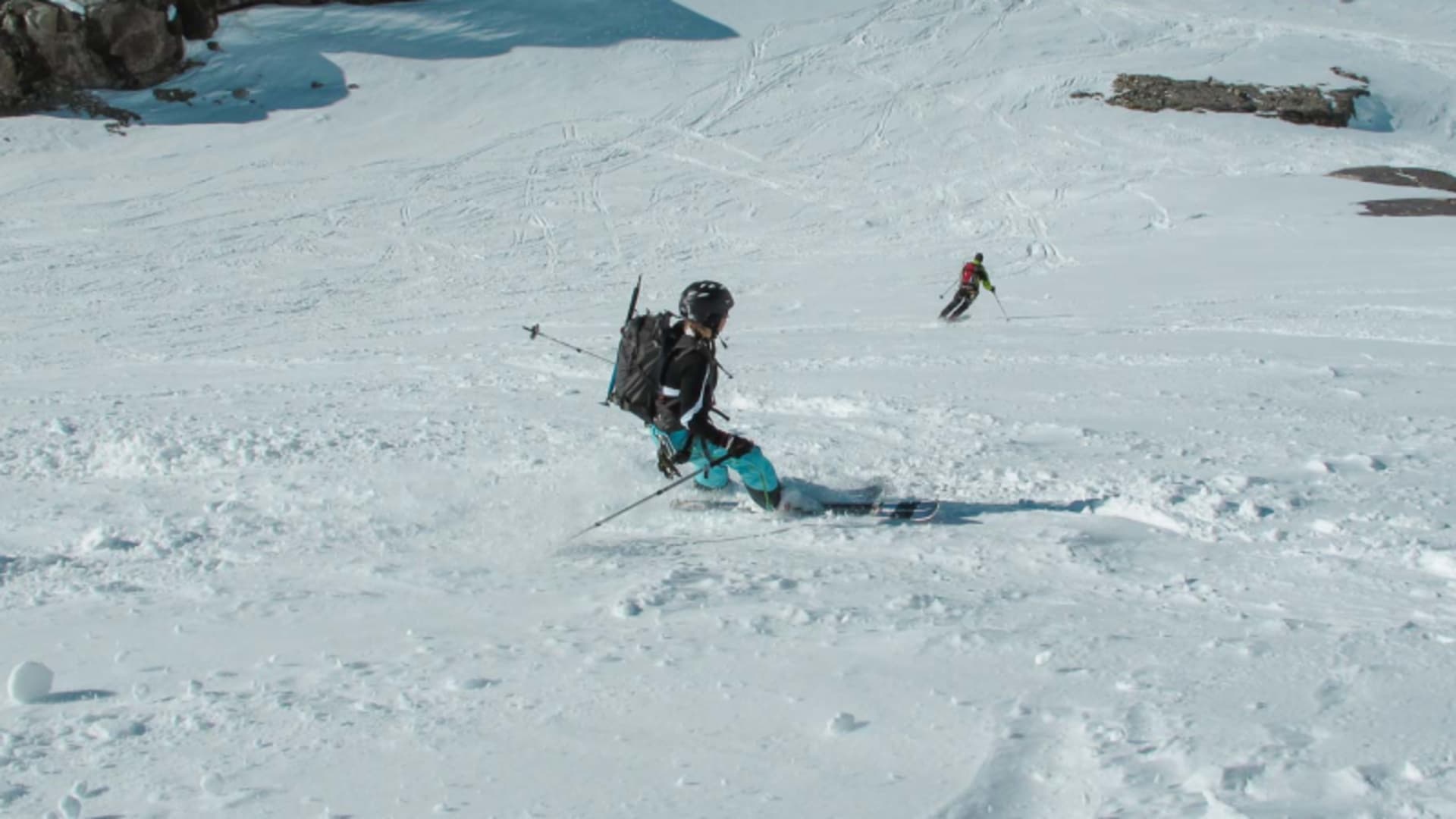 Zwei Skitourengeher fahren einen schneebedeckten Firn­hang am Großglockner ab, Schnee wirbelt auf.