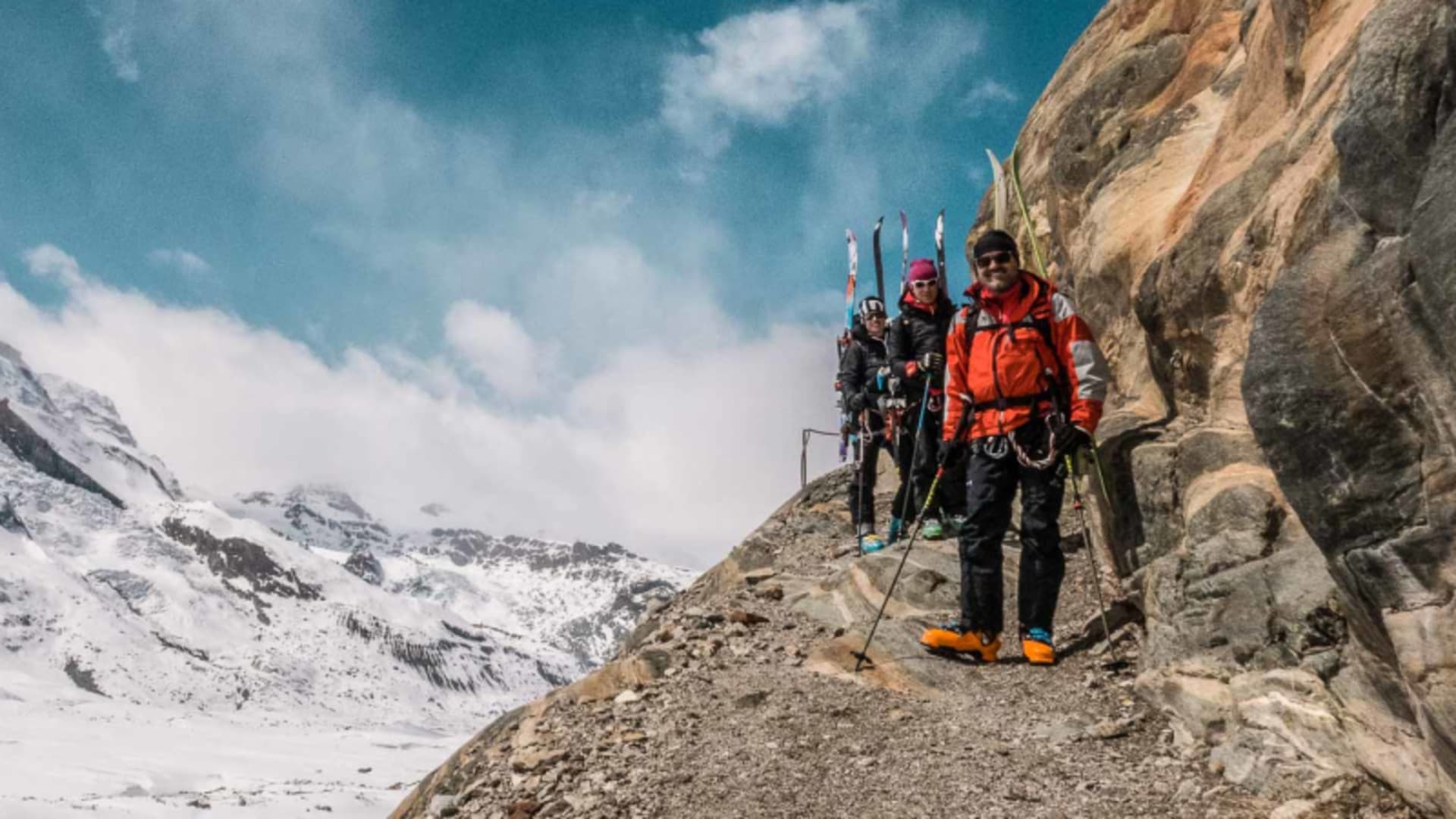 Drei Skitourengeher mit Ski am Rucksack pausieren auf felsigem Grat beim Abstieg zur Monterosahütte.