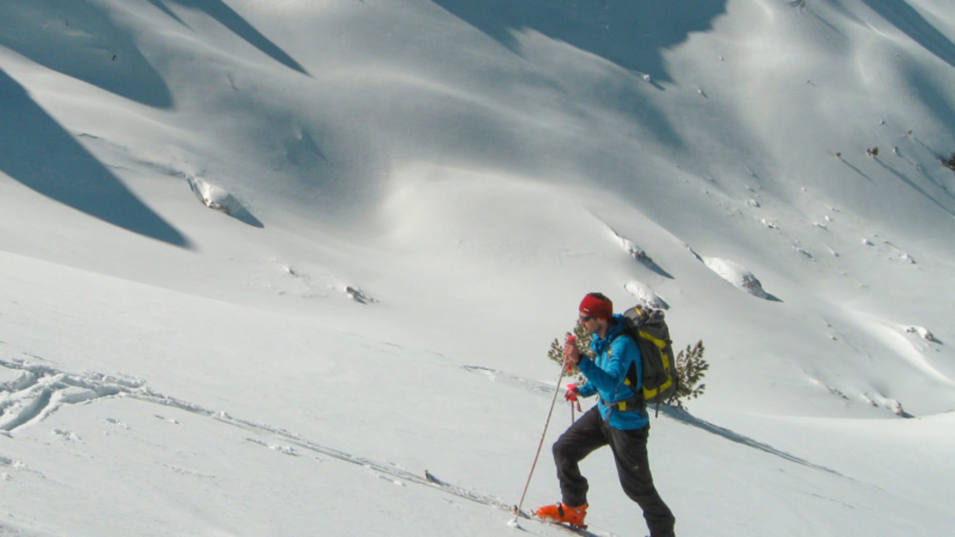 Ein Skitourengeher mit blauer Jacke und Fellen steigt einen tief verschneiten Hang in Montenegro
