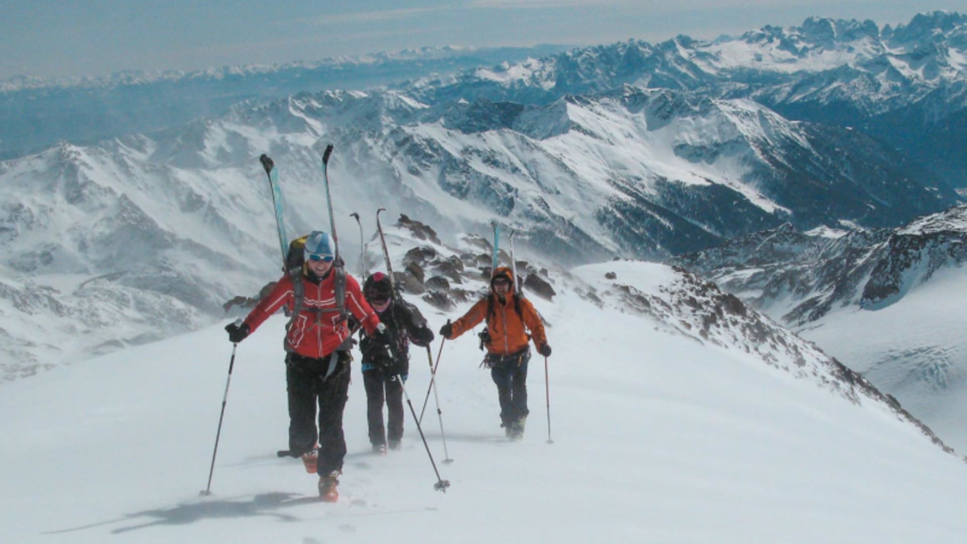 Drei Skitourengeher mit Fellen steigen einen verschneiten Hang im Ortlergebiet auf, Hochgebirgspanorama im Hintergrund.