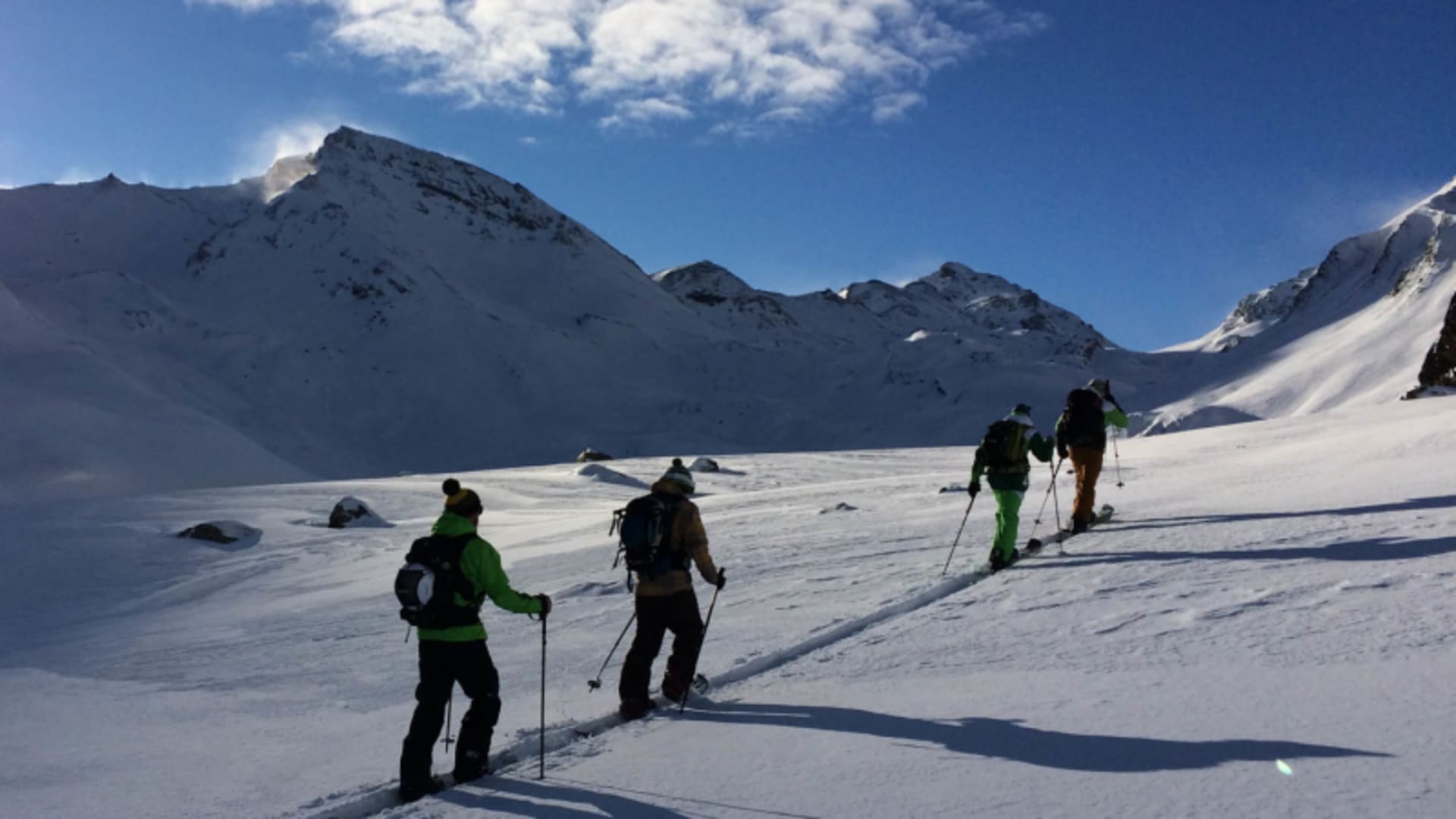 Vier Skitourengeher im Aufstieg auf verschneitem Hochplateau nahe der Heidelberger Hütte im Gegenlicht.