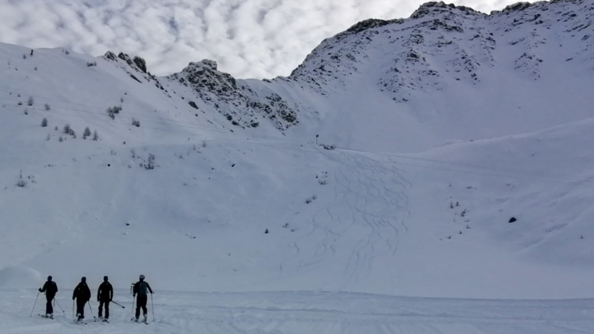 Vier Skitourengeher von hinten beim Aufstieg am Mont de Flassin auf verschneitem Kesselgelände im Winter.