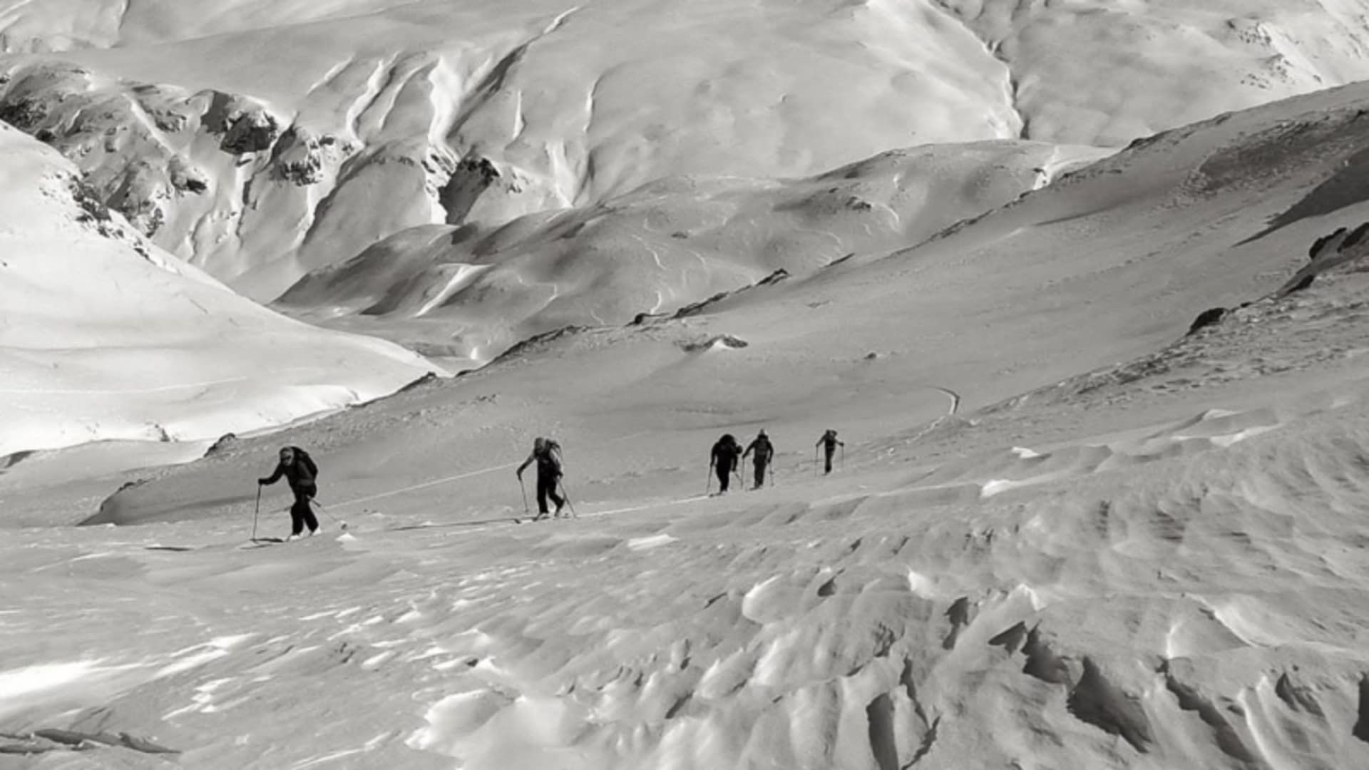 Fünf Skitourengeher steigen in lockerer Reihe den schneebedeckten Hang zum Piz Sesvenna auf.
