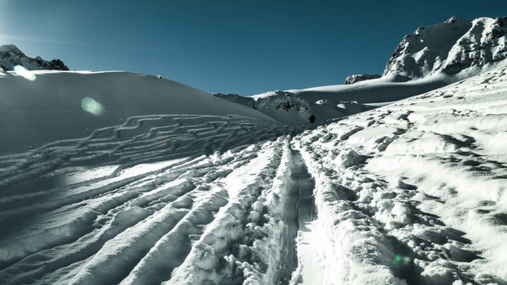 Ein Skitourengeher steigt auf einem Schneerücken in der Silvretta in Richtung Sattel auf, Gegenlicht.