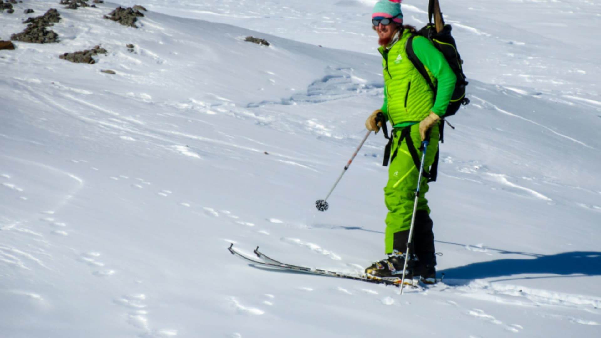 Skitourengeher mit Rucksack und Skistock auf schneebedecktem Hang in Spitzbergen.