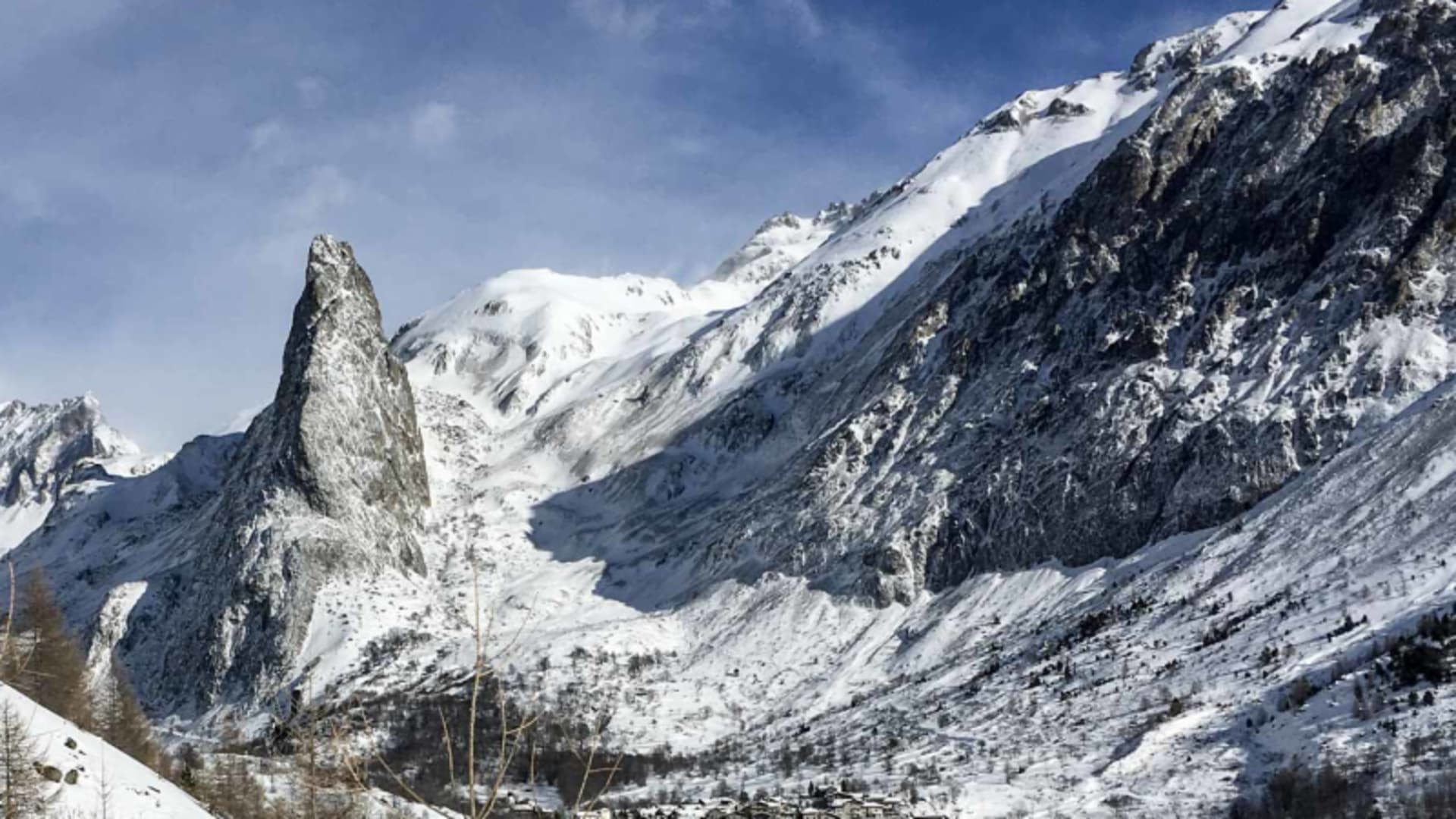 Skitour im Valle Maira: markante Felsnadel über schneebedecktem Tal mit Bergdorf im Piemont.