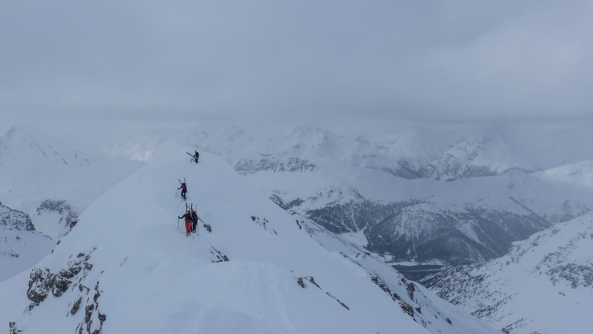 Drei Skitourengeher steigen mit Ski am Rücken einen schmalen Grat im Val Müstair auf.