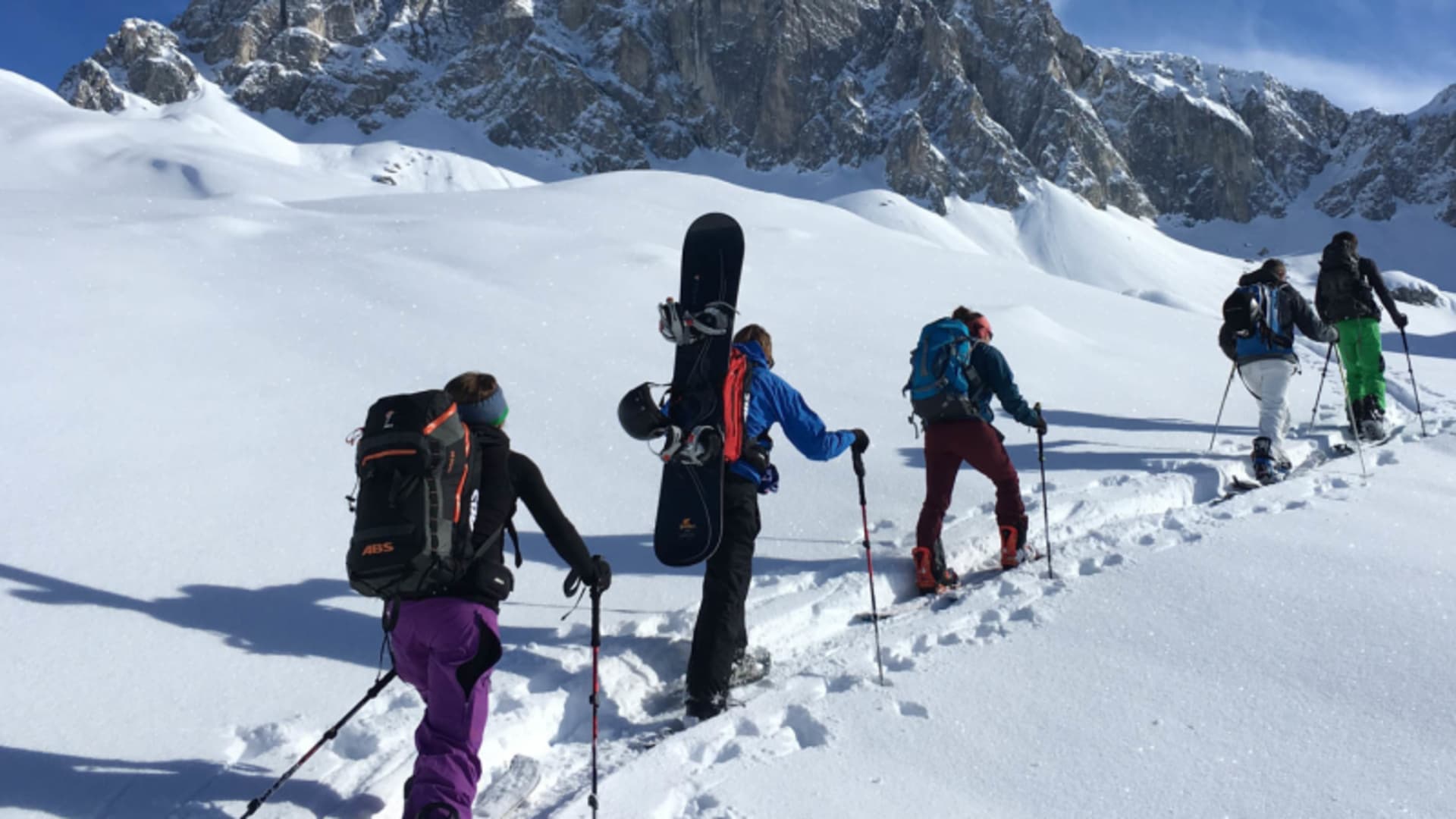 Fünf Skitourengeher steigen hintereinander einen verschneiten Hang vor einer steilen Felswand in der Silvretta auf.