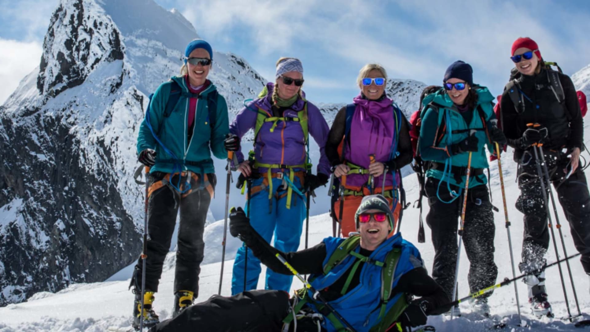 Sechs Skitourengeher als Gruppe im Jotunheimen, vor einem markanten Felsgipfel mit Schnee und blauem Himmel.