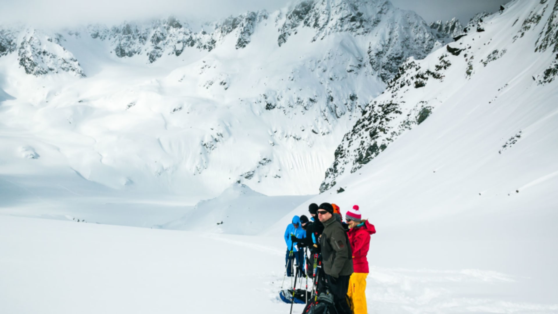 Vier Skitourengeher stehen auf einem Schneefeld in der Silvretta vor einem verschneiten Gebirgsstock.
