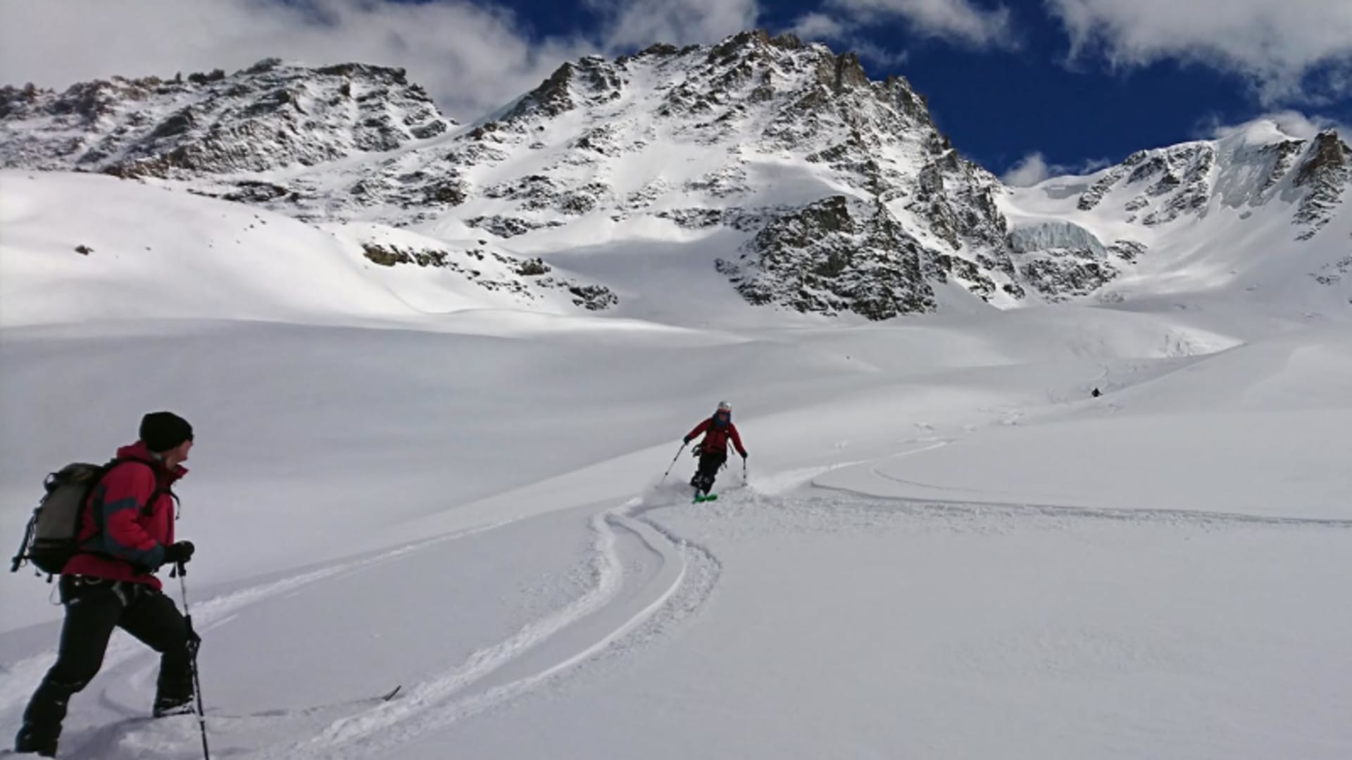 Zwei Skitourengeher auf weitem Schneeplateau am Gran Paradiso, im Hintergrund verschneite Felsgipfel und Gletschereis.