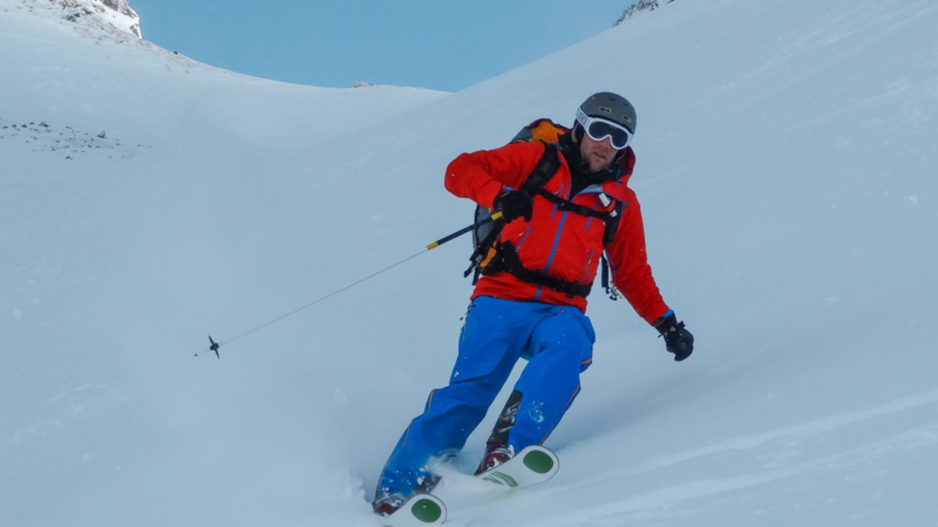 Freerider in roter Jacke fährt bei Skitour im Lötschental einen steilen schneebedeckten Hang mit blauem Himmel und felsigen Gipfeln
