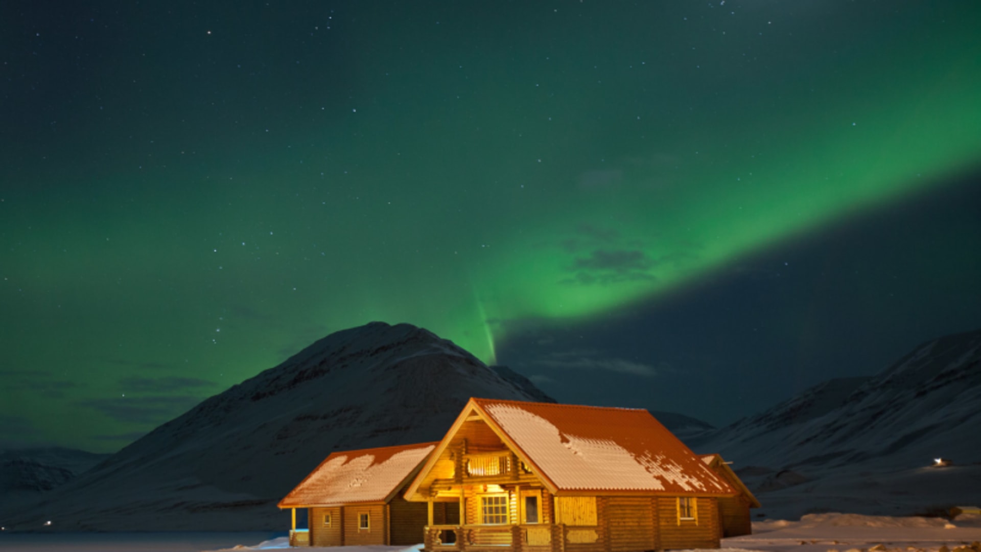 Aurora borealis über schneebedeckter Berglandschaft Island: beleuchtetes Blockhaus auf Skitour unter grünen Polarlichtern