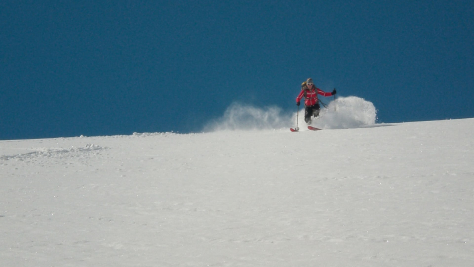 Skitourengeher fährt mit aufgewirbeltem Pulverschnee einen offenen Hang auf der Hoch Tirol ab.