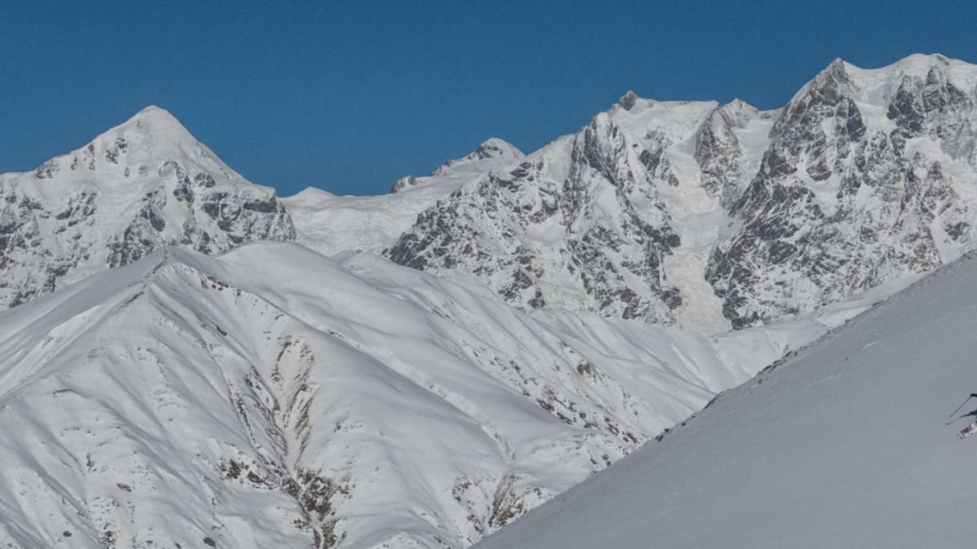 Skitourengeher fährt einen unverspurten Pulverschneehang in Swanetien ab, im Hintergrund vergletscherte Gipfel.