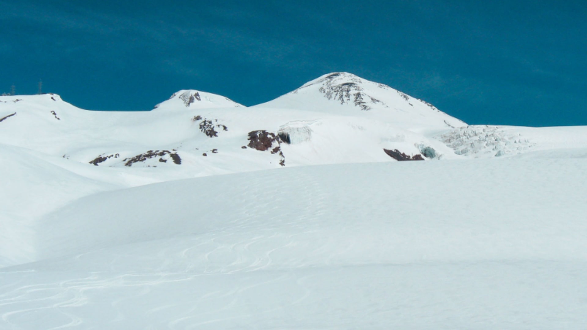 Skitour Russland: weitläufiges Schneefeld mit mehrgipfligem Bergmassiv, Felspartien und Gletscherzone mit Seracs im Hintergrund