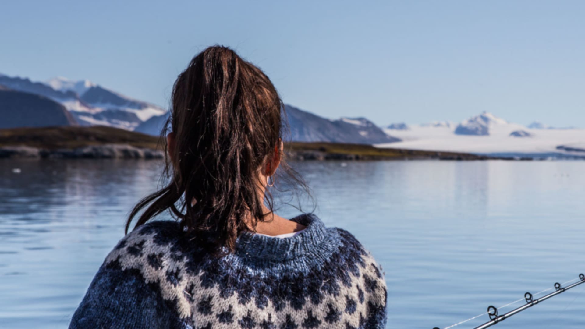 Person angelt am spiegelglatten Fjord auf Spitzbergen, Gletscher und Schneeberge im Hintergrund – Rahmenprogramm einer Skitour