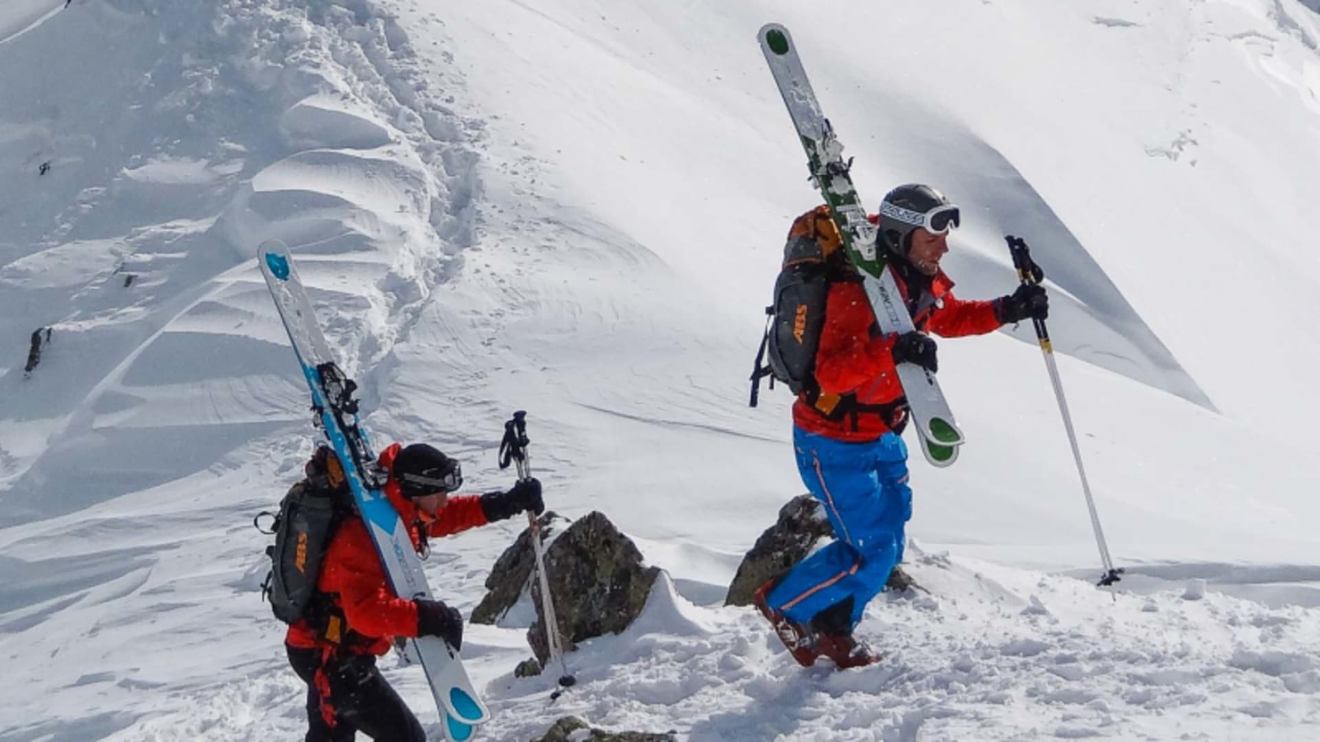 Zwei Freerider tragen ihre Ski beim Aufstieg einen verschneiten Steilhang in Andermatt hinauf.