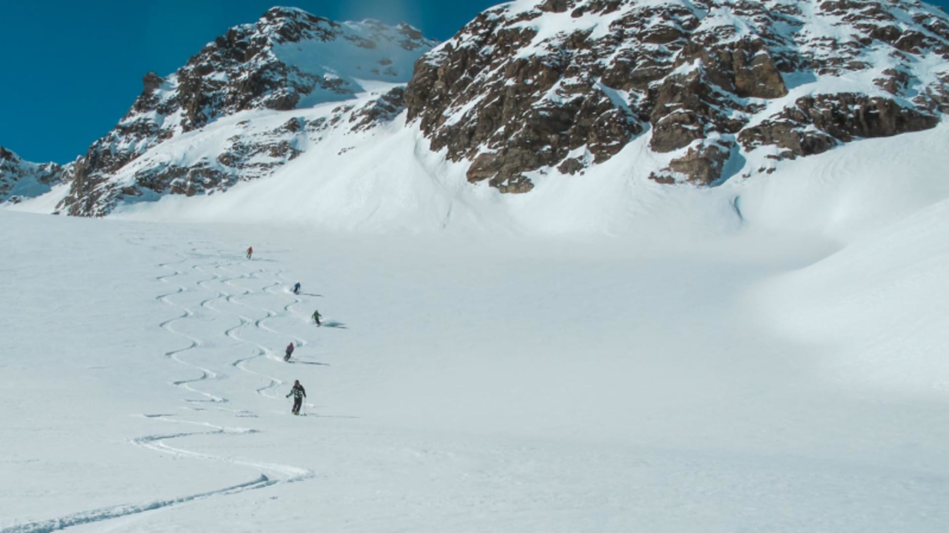 Fünf Skitourengeher fahren in der Silvretta einen unberührten Pulverschneehang mit Felsgipfel im Hintergrund ab.