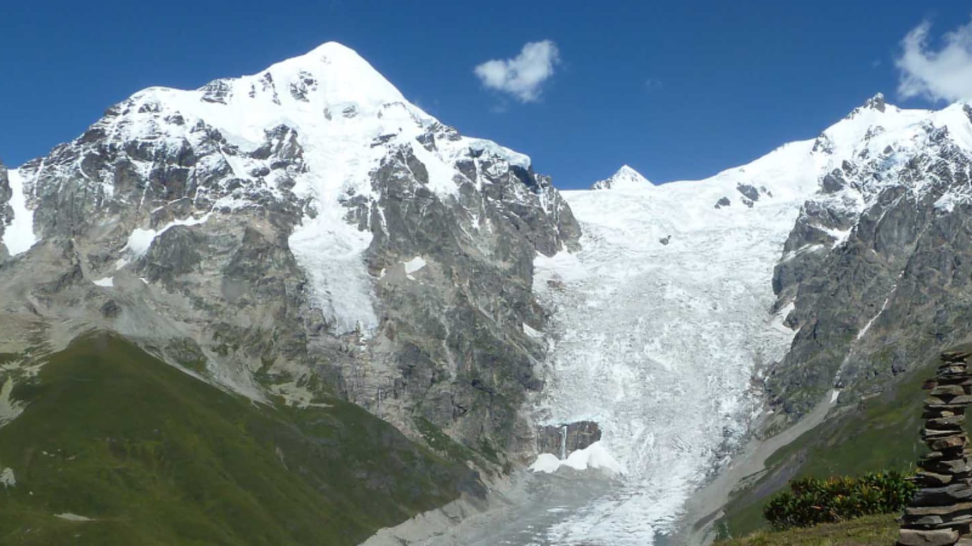 Trekking am Adishi Gletscher in Swanetien: Steinmann im Vordergrund, dahinter Gletscherzunge und grüne Hänge.
